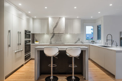This is an example of a mid-sized modern u-shaped open plan kitchen in Vancouver with an undermount sink, flat-panel cabinets, white cabinets, quartzite benchtops, white splashback, marble splashback, stainless steel appliances, light hardwood floors, with island and beige floor.