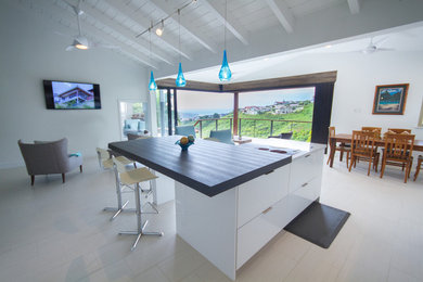 Example of a large trendy l-shaped ceramic tile eat-in kitchen design in Hawaii with an undermount sink, flat-panel cabinets, white cabinets, wood countertops, brown backsplash, paneled appliances and an island