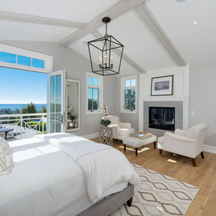 Großes Maritimes Hauptschlafzimmer mit grauer Wandfarbe, braunem Holzboden, Kamin, braunem Boden und gefliester Kaminumrandung in Los Angeles