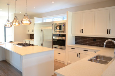 Inspiration for a modern l-shaped porcelain tile eat-in kitchen remodel in Calgary with an undermount sink, recessed-panel cabinets, white cabinets, brown backsplash, glass tile backsplash, stainless steel appliances, an island and quartz countertops