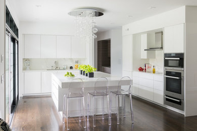 This is an example of a large contemporary l-shaped open plan kitchen in New York with an undermount sink, flat-panel cabinets, white cabinets, solid surface benchtops, white splashback, stone slab splashback, panelled appliances, dark hardwood floors and with island.