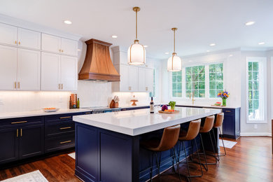 Inredning av ett klassiskt stort vit vitt kök, med en undermonterad diskho, skåp i shakerstil, blå skåp, bänkskiva i kvarts, vitt stänkskydd, stänkskydd i porslinskakel, rostfria vitvaror, mellanmörkt trägolv, en köksö och brunt golv