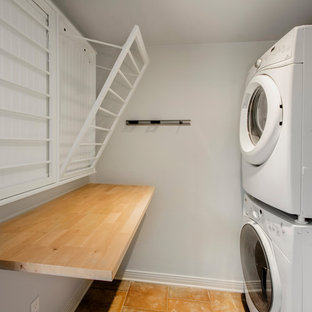 ダラスの中サイズのトラディショナルスタイルのおしゃれな洗濯室 (木材カウンター、グレーの壁、テラコッタタイルの床、上下配置の洗濯機・乾燥機、オレンジの床、茶色いキッチンカウンター) の写真