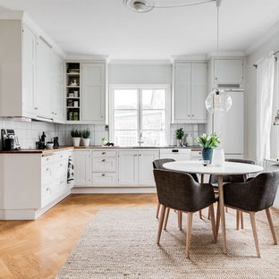 Idéer för att renovera ett avskilt skandinaviskt l-kök, med luckor med infälld panel, vita skåp, träbänkskiva, vitt stänkskydd, vita vitvaror, ljust trägolv och beiget golv