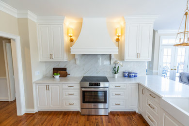Example of a classic medium tone wood floor and brown floor kitchen design in Other with raised-panel cabinets, white cabinets, quartz countertops, white backsplash, quartz backsplash, stainless steel appliances, a peninsula and white countertops