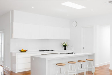 Design ideas for a small contemporary single-wall eat-in kitchen in Melbourne with an undermount sink, flat-panel cabinets, white cabinets, limestone benchtops, white splashback, glass sheet splashback, stainless steel appliances and with island.