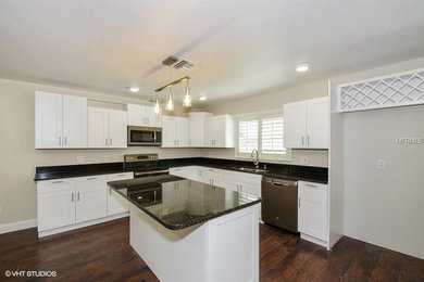 Example of a mid-sized transitional l-shaped dark wood floor and brown floor enclosed kitchen design in Orlando with a double-bowl sink, shaker cabinets, white cabinets, granite countertops, stainless steel appliances, an island and black countertops