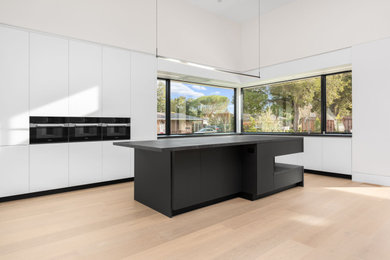 Photo of a large modern galley open plan kitchen in San Francisco with a submerged sink, flat-panel cabinets, white cabinets, engineered stone countertops, black appliances, an island and black worktops.