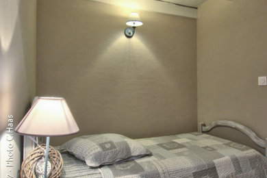 Cette photo montre une petite chambre d'amis nature avec un mur beige, sol en stratifié, un sol gris et poutres apparentes.