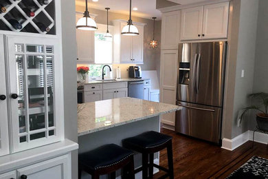 Eat-in kitchen - mid-sized traditional l-shaped medium tone wood floor eat-in kitchen idea in Baltimore with a double-bowl sink, recessed-panel cabinets, white cabinets, quartz countertops, white backsplash, stainless steel appliances and a peninsula