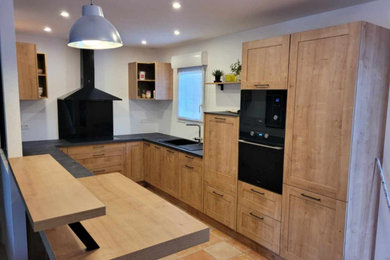 Ejemplo de cocinas en U moderno abierto con fregadero de un seno, puertas de armario de madera clara, electrodomésticos con paneles y encimeras negras
