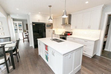 Eat-in kitchen - large transitional l-shaped medium tone wood floor and brown floor eat-in kitchen idea in Calgary with shaker cabinets, white cabinets, quartz countertops, white backsplash, an island, an undermount sink and black appliances