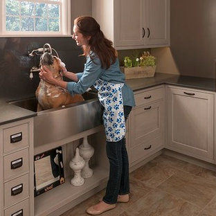 Medium sized contemporary l-shaped utility room in Houston with a belfast sink, beige cabinets, soapstone worktops, beige walls, ceramic flooring, a concealed washer and dryer, beige floors and beaded cabinets.