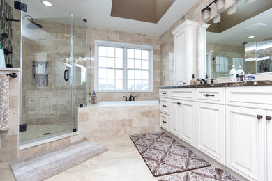 Large traditional master bathroom in DC Metro with raised-panel cabinets, white cabinets, a drop-in tub, a corner shower, beige tile, stone tile, porcelain floors, an undermount sink, granite benchtops, beige floor and a hinged shower door.