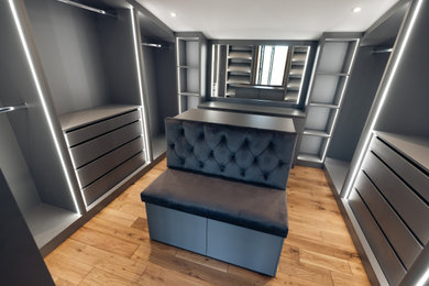Design ideas for a medium sized contemporary gender neutral dressing room in Buckinghamshire with open cabinets, grey cabinets, light hardwood flooring, brown floors and feature lighting.