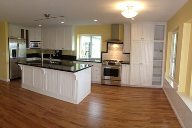 This is an example of a mid-sized traditional l-shaped eat-in kitchen in Sacramento with a double-bowl sink, shaker cabinets, white cabinets, white splashback, ceramic splashback, stainless steel appliances, medium hardwood floors, with island and brown floor.