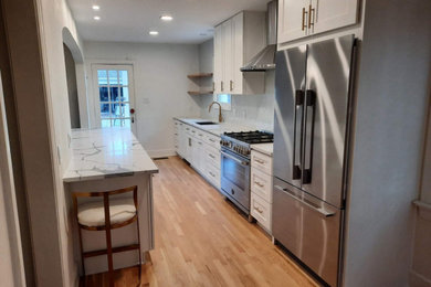 Example of a mid-sized french country galley light wood floor and multicolored floor eat-in kitchen design in Dallas with an undermount sink, shaker cabinets, white cabinets, quartzite countertops, white backsplash, glass tile backsplash, stainless steel appliances, an island and white countertops