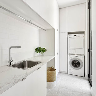 Design ideas for a modern l-shaped utility room in Melbourne with a built-in sink, flat-panel cabinets, white cabinets, a stacked washer and dryer, grey floors and white worktops.