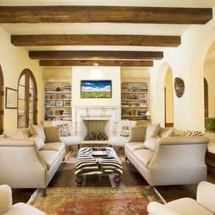 Ejemplo de salón cerrado, mediterráneo, grande, con paredes amarillas, suelo de madera oscura, chimenea tradicional, marco de chimenea de piedra, televisor colgado en la pared y suelo marrón