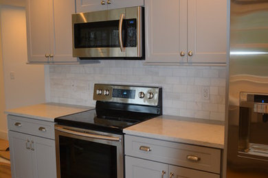 Mid-sized elegant galley medium tone wood floor eat-in kitchen photo in Boston with a farmhouse sink, shaker cabinets, gray cabinets, granite countertops, gray backsplash, ceramic backsplash, stainless steel appliances and a peninsula