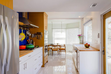 Mid-century modern galley porcelain tile and white floor eat-in kitchen photo in Other with an undermount sink, flat-panel cabinets, light wood cabinets, wood countertops, green backsplash, glass sheet backsplash, stainless steel appliances, no island and white countertops