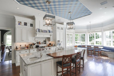 Eat-in kitchen - large traditional galley medium tone wood floor and brown floor eat-in kitchen idea in New York with a farmhouse sink, beaded inset cabinets, white cabinets, marble countertops, white backsplash, subway tile backsplash, stainless steel appliances and an island