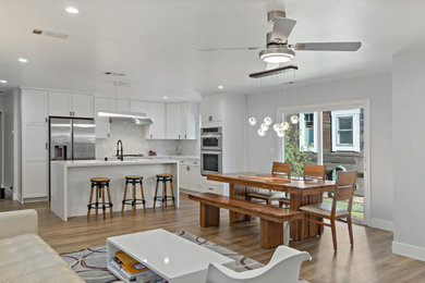 Expansive modern l-shaped eat-in kitchen in San Francisco with an undermount sink, shaker cabinets, white cabinets, quartzite benchtops, white splashback, stainless steel appliances, laminate floors, with island and white benchtop.