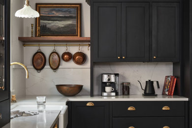 ポートランド(メイン)にある高級な中くらいなトラディショナルスタイルのおしゃれなL型キッチン (エプロンフロントシンク、黒いキャビネット、クオーツストーンカウンター、白いキッチンパネル、クオーツストーンのキッチンパネル、黒い調理設備、淡色無垢フローリング、白いキッチンカウンター、シェーカースタイル扉のキャビネット、ベージュの床) の写真