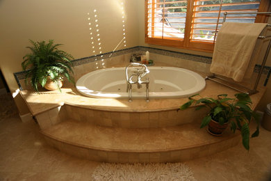 Drop-in bathtub - mid-sized mediterranean 3/4 travertine floor drop-in bathtub idea in Orange County with raised-panel cabinets, medium tone wood cabinets, beige walls, an undermount sink and marble countertops