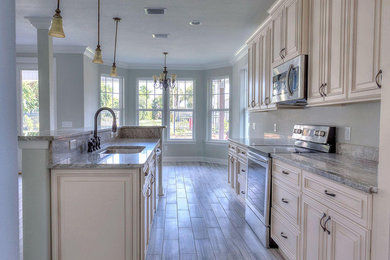Example of a mid-sized classic galley porcelain tile and brown floor enclosed kitchen design in Miami with raised-panel cabinets, white cabinets, quartzite countertops, stainless steel appliances, gray countertops and an island