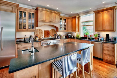 Inspiration for a mid-sized traditional l-shaped eat-in kitchen in New York with an undermount sink, shaker cabinets, medium wood cabinets, granite benchtops, stainless steel appliances, medium hardwood floors, with island, brown floor and black benchtop.