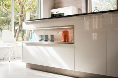 Inspiration for a small contemporary l-shaped separate kitchen in Miami with an undermount sink, flat-panel cabinets, white cabinets, quartz benchtops, orange splashback, stone slab splashback, stainless steel appliances, concrete floors, a peninsula, grey floor and black benchtop.