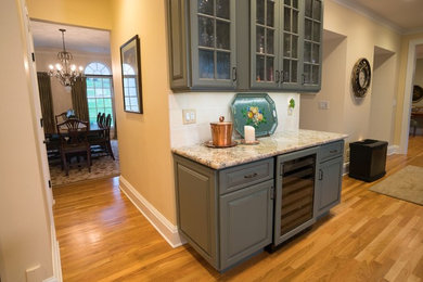 Inspiration for a large timeless l-shaped medium tone wood floor eat-in kitchen remodel in New York with raised-panel cabinets, green cabinets, granite countertops, beige backsplash, ceramic backsplash and an island
