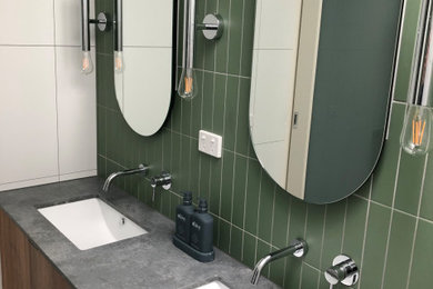 Photo of a small contemporary master bathroom in Other with brown cabinets, an open shower, green tile, ceramic tile, green walls, ceramic floors, an undermount sink, solid surface benchtops, black floor, grey benchtops, a double vanity, flat-panel cabinets and a floating vanity.