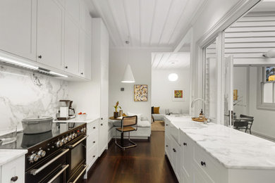 This is an example of a mid-sized traditional galley eat-in kitchen in Auckland with a farmhouse sink, shaker cabinets, white cabinets, white splashback, no island and white benchtop.
