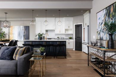 Inspiration for a large transitional single-wall eat-in kitchen in Toronto with an undermount sink, shaker cabinets, white cabinets, quartz benchtops, white splashback, ceramic splashback, white appliances, light hardwood floors, with island, white floor and black benchtop.