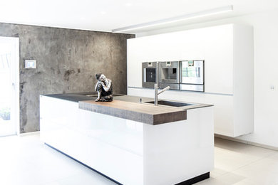 This is an example of a contemporary open plan kitchen in Stuttgart with a drop-in sink, flat-panel cabinets, white cabinets, stainless steel appliances, concrete floors and with island.