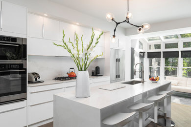 Large trendy light wood floor open concept kitchen photo in Toronto with an undermount sink, flat-panel cabinets, white cabinets, quartz countertops, white backsplash, stone slab backsplash, stainless steel appliances, an island and white countertops