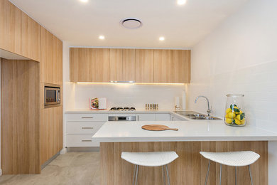 This is an example of a mid-sized u-shaped separate kitchen in Sydney with a double-bowl sink, white splashback, subway tile splashback, stainless steel appliances, light wood cabinets, laminate benchtops and a peninsula.