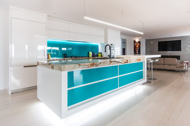 Design ideas for an expansive modern galley open plan kitchen in Auckland with a double-bowl sink, white cabinets, quartzite benchtops, green splashback, glass sheet splashback, white appliances, light hardwood floors and with island.