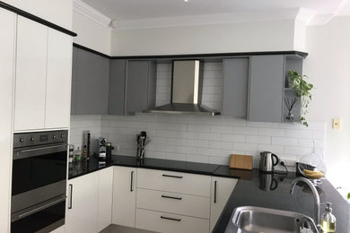 Photo of a mid-sized modern u-shaped kitchen pantry in Gold Coast - Tweed with a drop-in sink, white cabinets, quartz benchtops, white splashback, subway tile splashback, stainless steel appliances, porcelain floors, beige floor and black benchtop.