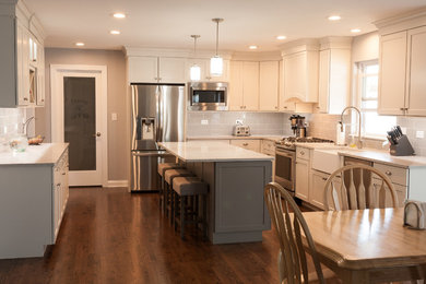 Large transitional u-shaped eat-in kitchen in Chicago with a farmhouse sink, shaker cabinets, white cabinets, grey splashback, subway tile splashback, stainless steel appliances, dark hardwood floors, with island, brown floor and marble benchtops.