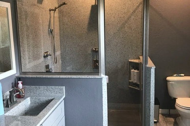 Inspiration for a mid-sized transitional master laminate floor and gray floor corner shower remodel in Denver with shaker cabinets, gray cabinets, a two-piece toilet, gray walls, an integrated sink, laminate countertops, a hinged shower door and gray countertops