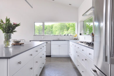 Mid-sized contemporary u-shaped open plan kitchen in Other with a single-bowl sink, white cabinets, white splashback, porcelain splashback, stainless steel appliances, concrete floors, with island, grey floor and black benchtop.