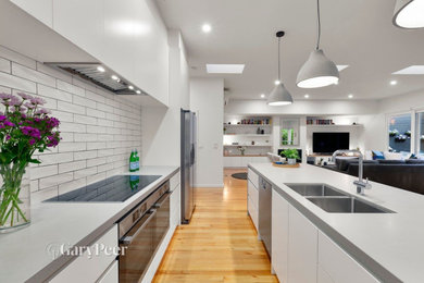 Inspiration for a galley kitchen in Melbourne with a double-bowl sink, white cabinets, white splashback, ceramic splashback, black appliances, with island and grey benchtop.