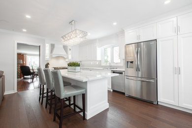 Example of a large transitional l-shaped medium tone wood floor and brown floor enclosed kitchen design in Toronto with an undermount sink, recessed-panel cabinets, white cabinets, quartz countertops, gray backsplash, ceramic backsplash, stainless steel appliances, an island and white countertops