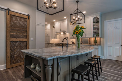 This is an example of a large country galley eat-in kitchen in Other with a farmhouse sink, raised-panel cabinets, white cabinets, white splashback, mosaic tile splashback, stainless steel appliances, laminate floors, with island, brown floor, grey benchtop and granite benchtops.