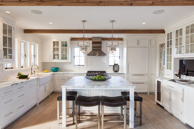 Large beach style u-shaped light wood floor kitchen photo in Boston with a farmhouse sink, white cabinets, marble countertops, white backsplash, subway tile backsplash, paneled appliances, an island and shaker cabinets