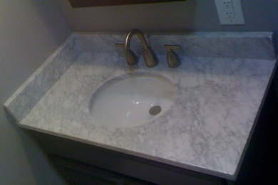 Small trendy powder room photo in San Diego with an undermount sink, raised-panel cabinets, dark wood cabinets, marble countertops and gray walls