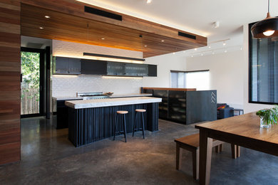 Contemporary kitchen in Melbourne with glass-front cabinets, black cabinets, white splashback, subway tile splashback, stainless steel appliances, concrete floors and with island.